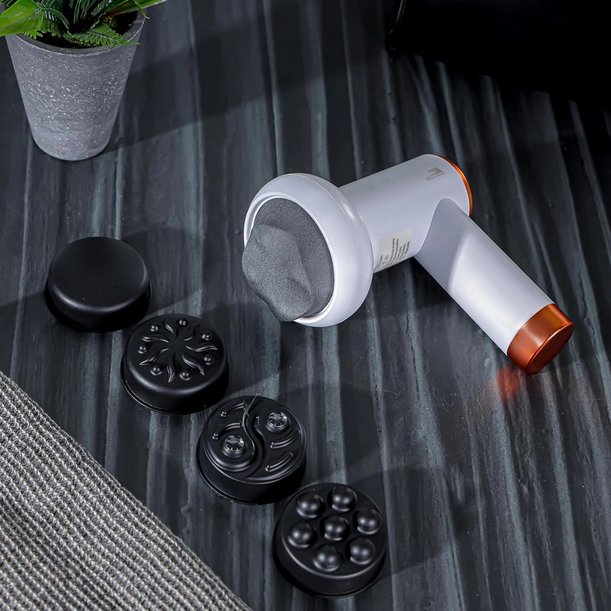 SKY LAND EM-4139 cordless handheld massage gun with interchangeable massage heads displayed on a tabletop for deep tissue massage, muscle recovery, body relaxation, and cellulite care.